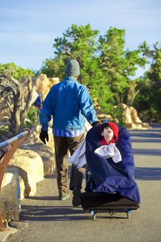 Father pulling disabled little boy in wheelchair backwards at Grand Canyon