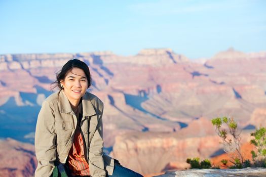 Young biracial  teen girl sitting on rocky edge at Grand Canyon, smiling