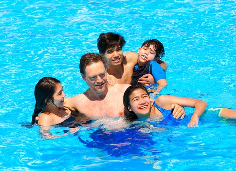 Multiracial family swimming together in pool. Disabled youngest son has cerebral palsy.