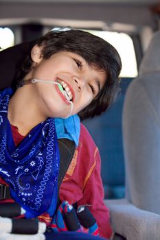 Disabled biracial eight year old boy sitting in carseat inside vehicle, smiling. Child has cerebral palsy.