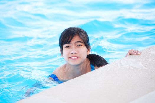Young biracial Asian teen girl relaxing in pool, smiling at camera