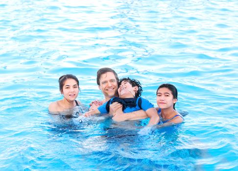 Multiracial family swimming together in pool. Disabled youngest son has cerebral palsy.