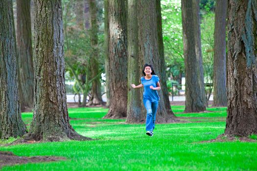 Young teen biracial Asian  girl walking under tall trees, on bright green grass