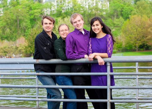 Four young multiethnic friends in early twenties standing  together along metal railing by lake