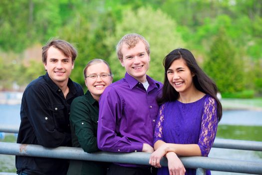 Four young multiethnic friends in early twenties standing  together along metal railing by lake