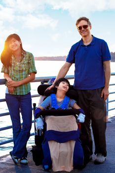 Disabled biracial child in wheelchair outdoors by lake with family. he has cerebral palsy.