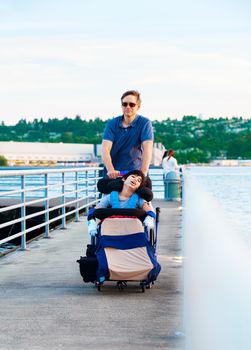 Disabled biracial child in wheelchair outdoors by lake with family. he has cerebral palsy.