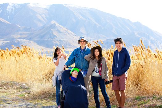 Caucasian father standing by field of tall grasses with biracial children. Youngest child in wheelchair has cerebral palsy.