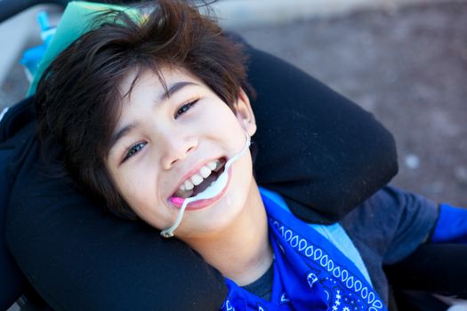 Handsome biracial disabled boy in wheelchair, smiling up at camera