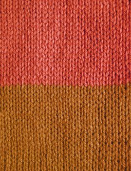 Length of stockinette stitch knitting in salmon pink and brown wool as an abstract background texture