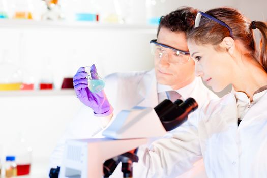 Chemical laboratory. Attractive young PhD student and her post doctoral supervisor scientist observing the blue indicator color shift after the solution  destillation.