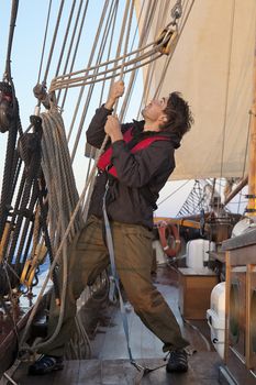 Young sailor on a ship's deck hoisting a sail