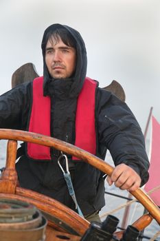 Young sailor on a ship's deck behind a steering wheel