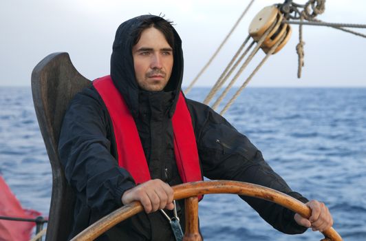 Young sailor on a ship's deck behind a steering wheel