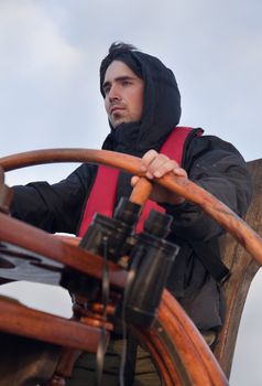 Young sailor on a ship's deck behind a steering wheel