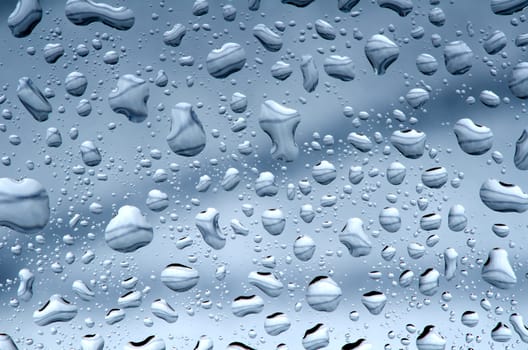 Water drops against blue gray background, wet glass surface.