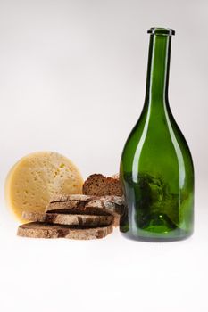 Cheese, pieces of bread and green bottle on isolated background