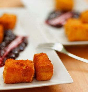 Breaded and Fried Camembert Cheese Served with Cranberry Jam on Blurred Plate and Fork background. Focus on Foreground 