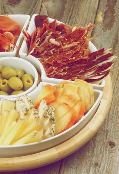 Spanish Snacks with Various Cheeses, Jamon, Cured Ham and Green Olives on Serving Plate closeup on Wooden background. Retro Styled