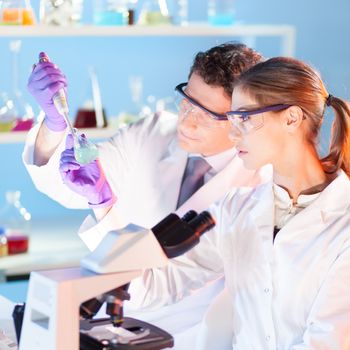 Chemical laboratory. Attractive young PhD student and her post doctoral supervisor scientist observing the blue indicator color shift after the solution  destillation.