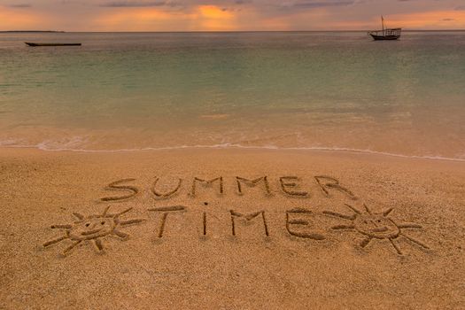 In the picture a beach at sunset with the words on the sand "Summer time" .