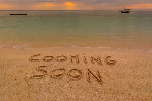 In the picture a beach at sunset with the words on the sand "Cooming soon".