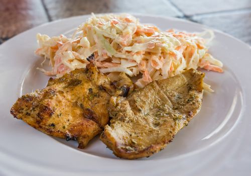 Pictured fillets grilled chicken with salad made from carrots, sauerkrauts and mayonnaise served on white plate.