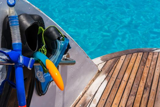 In the pictured boat with curved wooden deck wet,on the left  fins,mask,scuba rubber for snorkeling and in the background ocean blue / turquoise.