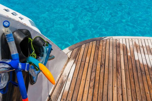 In the pictured boat with curved wooden deck wet,on the left  fins,mask,scuba rubber for snorkeling and in the background ocean blue / turquoise.