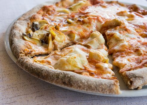 In the pictured a cut pizza with tomato, mozzarella, mushrooms, ham and artichokes.
