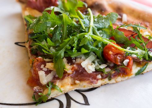 In the picture Italian pizza close-up with Arcula,cherry tomato,tomato,mozzarella,cheese,parmesan and Bresaola.