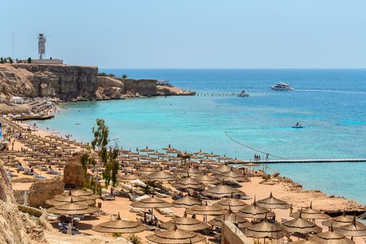 In the picture a typical Egyptian beach in the Red Sea with wood and straw umbrellas and turquoise sea.