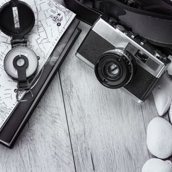 In the picture an analog camera film , a compass,book  and a map, on the sides shells and decorative stones .