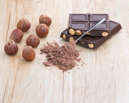 A front view of chocolate, hazelnuts and covered teaspoon cocoa.