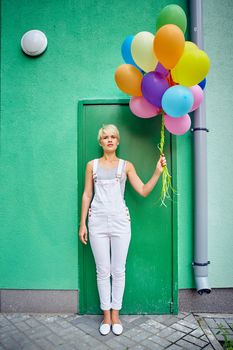 Happy young woman with colorful latex balloons on green background, outdoor