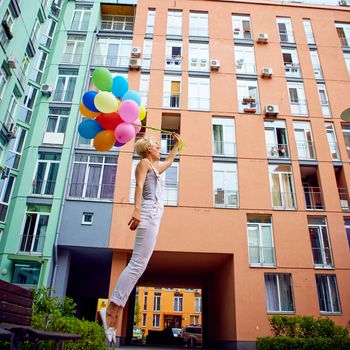 Happy young woman with colorful latex balloons, outdoor, jumping