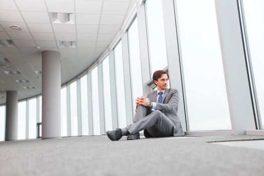 Businessman sitting on floor in office near window