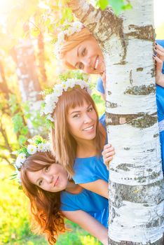 cheerful girl looks out from behind a birch trunk