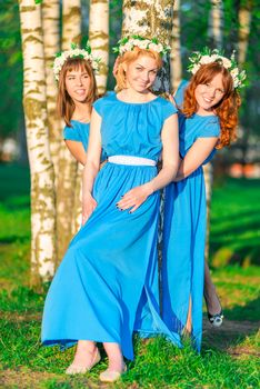 Girls in blue dresses with wreaths on heads posing near the birch