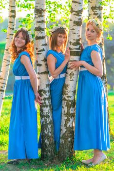 Three beautiful girls in blue dresses in the park on a sunny day