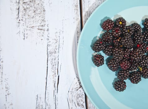 Blackberries on blue plate on wooden background