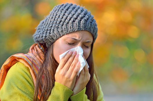 Girl in fall autumn park sneezing in tissue.