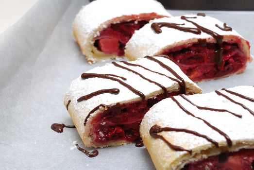 Swiss rolls (cake) )with cherry and strawberry decorated decorated with chocolate on parchment