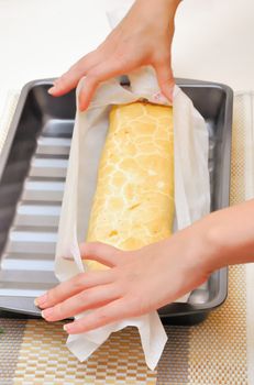 hands expand Swiss roll (cake) from parchment  in oven