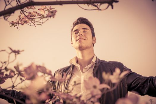 Good looking male model at couuntryside, among flowers, enjoying nature with eyes closed