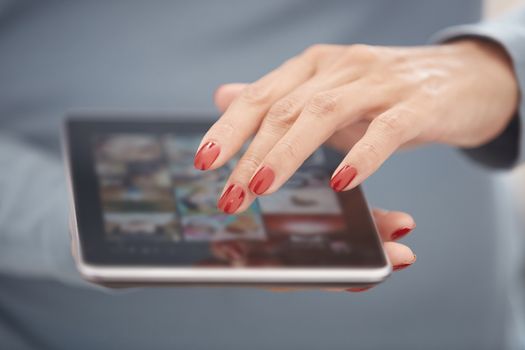 Woman with red manicure using tablet computer. Horizontal photo