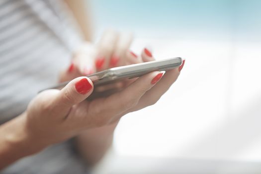 Woman with red manicure using smartphone. Horizontal photo
