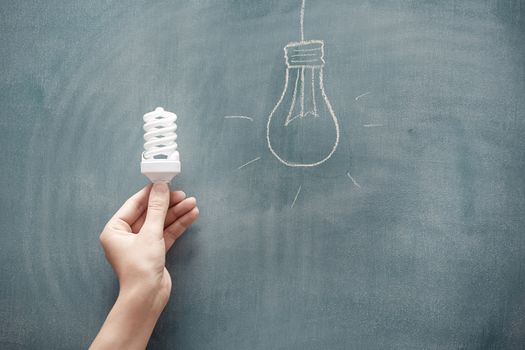 Human hand holding energy saving lamp at the blackboard