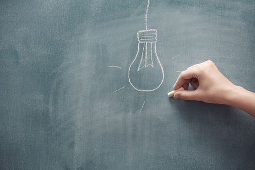 Human hand drawing electric lamp on a blackboard