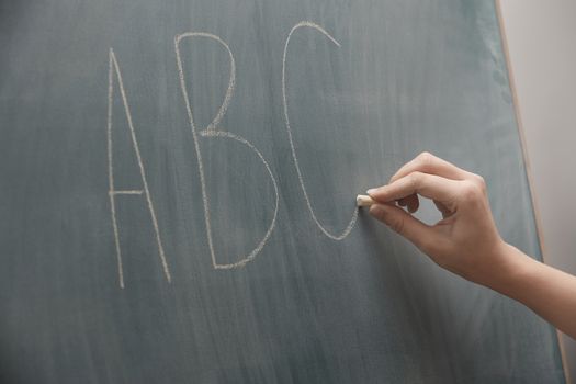 Human hand writing ABC characters on a blackboard